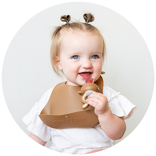 Baby girl using the Forage Feeder and wearing a silicone bib