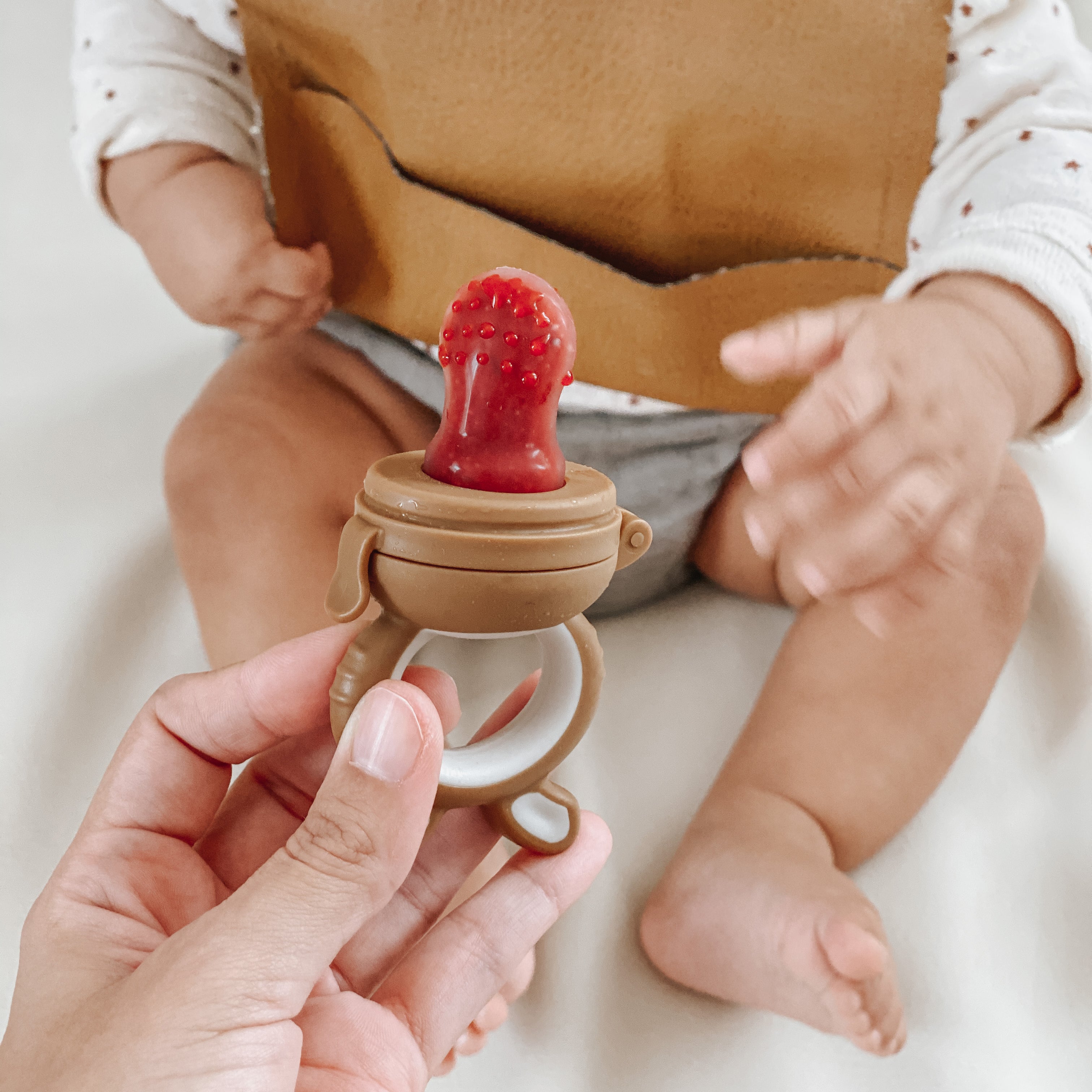 Mom handing reusable baby mesh teething feeder for fresh fruit snacks to baby